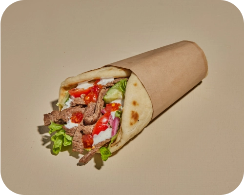 Steak shawarma with cucumber, tomato, lettuce, and sauces wrapped in a pita.